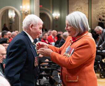 Governor General Mary Simon pinning a poppy to a veteran’s suit jacket.